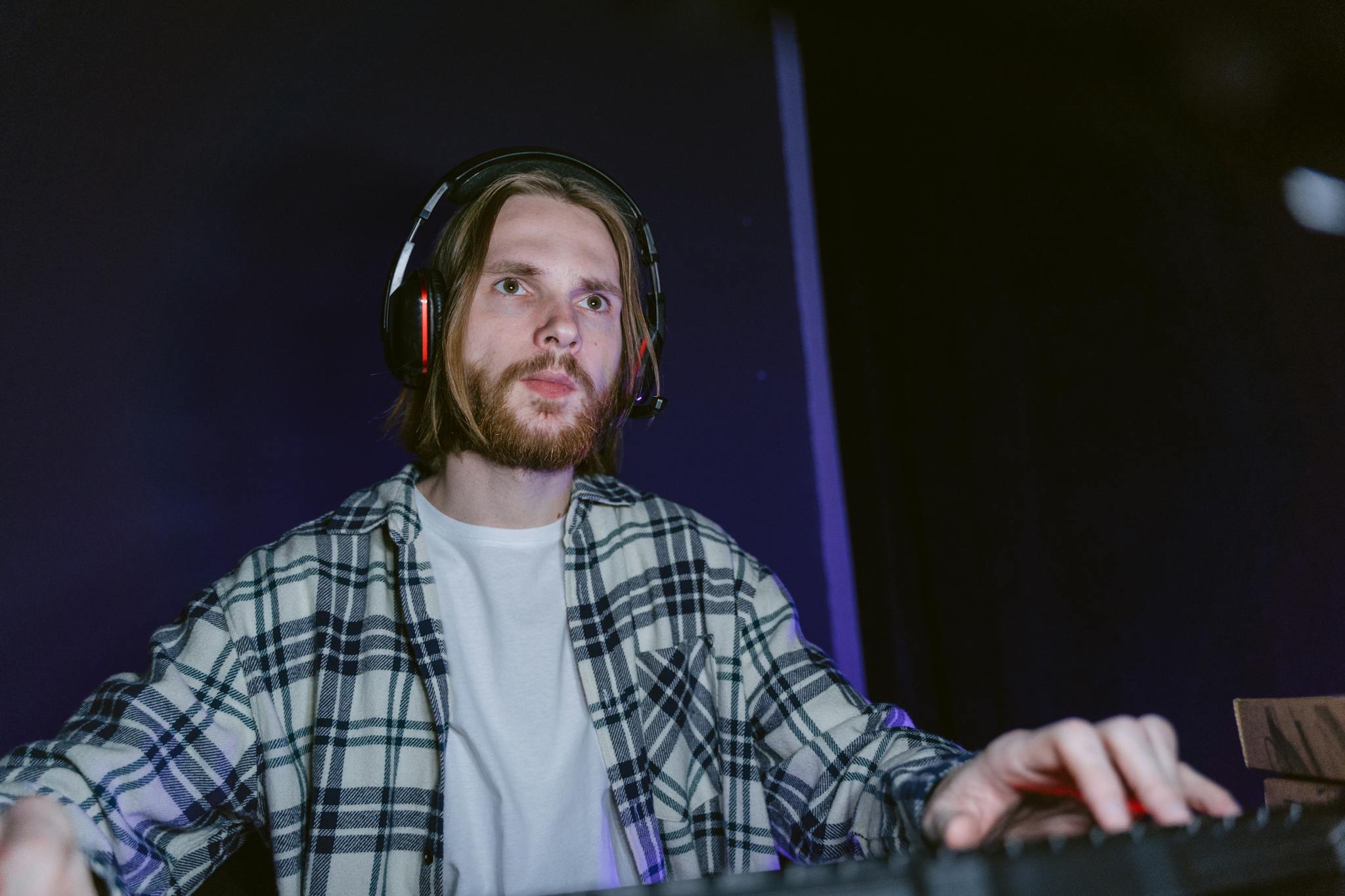 A man in a plaid shirt wearing a headset immersed in gaming, showcasing focus and leisure.